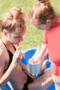 Teenage girl with her little sister spending time in the swimming pool enjoy eating ice cream on a summer day