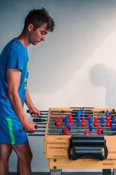 Young teenager boy playing table football with another player. Young people having fun, spending time together
