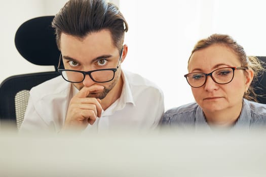 Two business people discussing financial data looking at computer screen. Entrepreneurs working hard sitting at computere screen in office. People having deadline working together. Workmates talking about project