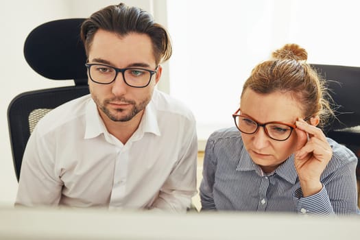 Two business people discussing financial data looking at computer screen. Entrepreneurs working hard sitting at computere screen in office. People having deadline working together. Workmates talking about project