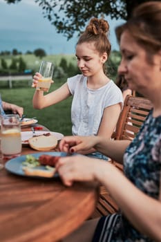 Family having a meal from grill during summer picnic outdoor dinner in a home garden. Close up of people sitting at a table with food and dishes