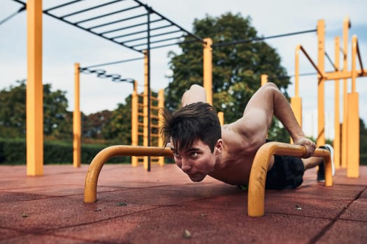 Young shirtless man bodybuilder doing push-ups on a parallel bars during his workout in a modern calisthenics street workout park