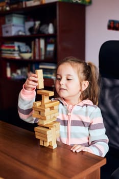 Little girl preschooler playing with wooden blocks toy building a tower. Concept of building a house