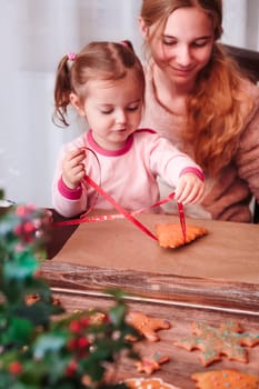 Girls tying baked Christmas gingerbread cookies with ribbon