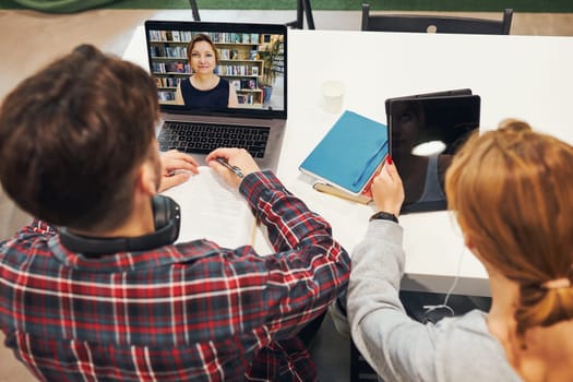Students learning in university library. Young man having video class on laptop. Girl writing essay and making notes using computer. Focused students studying for college exams. Back to school