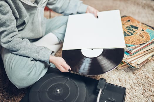 Young woman listening to music from vinyl record player. Retro and vintage music style. Girl holding analog record album sitting in room at home. Female enjoying music from old record collection