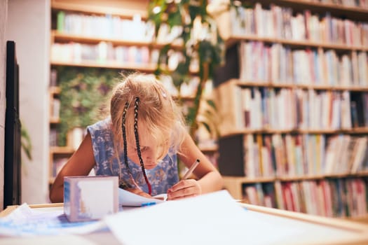 Schoolgirl doing homework. Elementary student learning, drawing pictures, doing puzzles at desk in school library. Primary student in school club. Smart girl learning from book