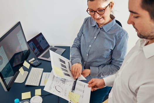 Woman entrepreneur discussing financial data with her colleague standing at desk in office. Happy positive businesswoman working with charts and tables. Two people working together. Workmates talking about project