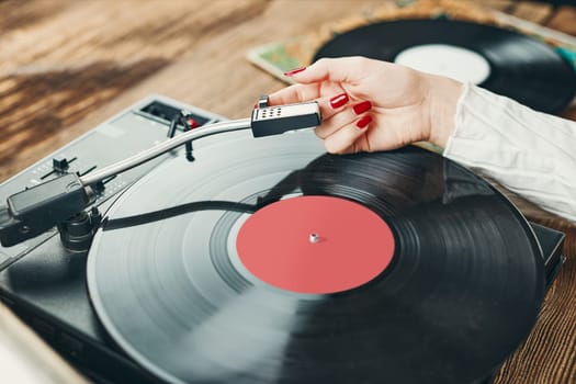 Young woman listening to music from vinyl record player. Playing music on turntable player. Female enjoying music from old record collection at home. Stack of analog vinyl records. Retro and vintage music style. Music Passion and hobby