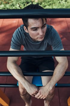 Portrait of young man having break during his workout in a modern calisthenics street workout park. Man sitting on a sit-up board wearing sportswear looking away