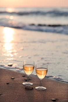 Two wine glasses with white wine standing on sand on beach