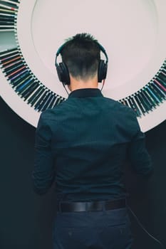 Young man listening to music through headphones standing next to bookshelf with recordings