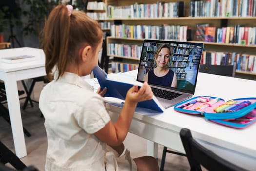 Student litttle girl having video class remotely with her teacher on laptop sitting at desk in after school club at primary school. Back to school. Child using technology on elementary computer science lesson. Smart little girl learning online. Teacher teaching remotely. E-learning classes