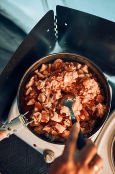 Close up of female hands putting dish with tomato sauce. Woman cooking meal on electric stove on camping during summer vacations. Camping life, preparing a meal