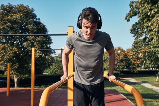 Young man doing dips on parallel bars during his workout in a modern calisthenics street workout park. Man listening to music wearing headphones and sportswear