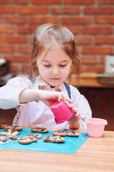 Little girl decorating her baked cookies with colorful sprinkle and icing sugar. Kid taking part in baking workshop. Baking classes for children,  aspiring little chefs. Learning to cook. Combining and stirring prepared ingredients. Real people, authentic situations