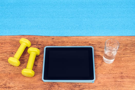 Tablet, dumbbells, glass of water prepared for workout with video fitness course