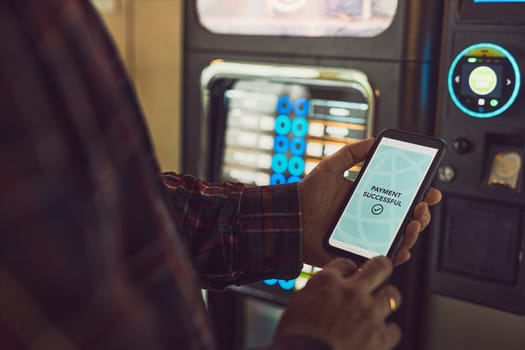 Consumer paying for product at vending machine using contactless method of payment with mobile phone. Man using payment app on smartphone to buy product. Male hand holding smart phone with payment confirmation on screen