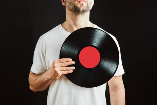 Man holding vinyl record over heart. Music passion. Vintage music style. Male holding old vinyl disk standing on black background. Retro music. Tribute to music
