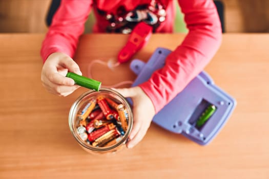 Little girl removing used batteries from toy and putting into jar for recycling. Child separating waste. Batteries only container