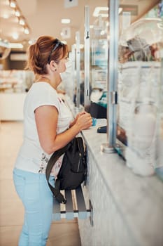 Woman shopping at pharmacy, buying medicines, wearing face mask to cover mouth and nose during pandemic coronavirus outbreak