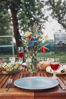 Dinner in an apple orchard garden on wooden table with salads and wine decorated with flowers. Close up of table with food prepared for family dinner