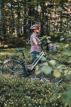 Active woman spending free vacation time on a bicycle trip in a forest on sunny summer day. Woman wearing bicycle helmet and gloves holding bike with basket standing behind the blurred tree leaves