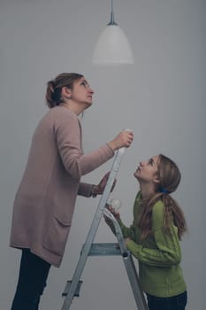 Woman and her daughter changing a light bulb together in dark room