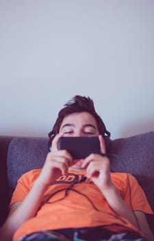 Boy using smart phones, listening to music, playing the games sitting on a couch at home