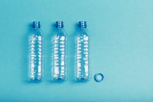 Empty plastic bottle, cup and cap over blue background. Collecting plastic waste to recycling. Concept of plastic pollution and too many plastic waste. Copy space at the top