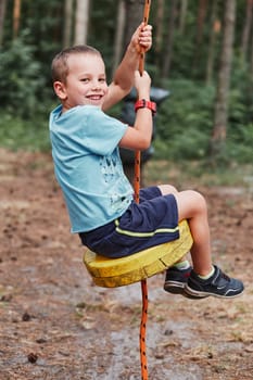 Happy boy riding on the zip line in rope park in forest while spending summer vacation. Real people, authentic situations