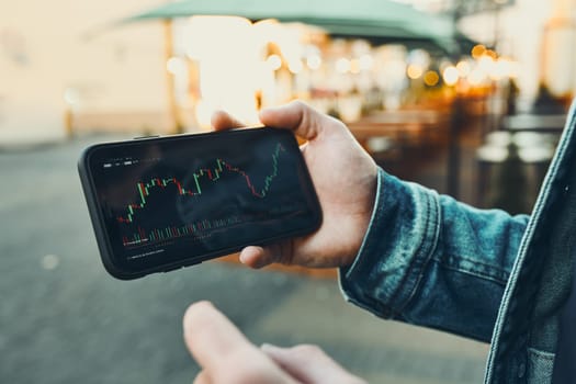 Person investing trading on stock cryptocurrency market using investing application on smartphone. Stock market investment in hand. Trader holding mobile phone looking at candle chart