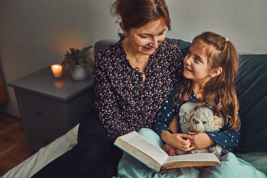 Mother reading book her daughter in bed before going to sleep. Reading stories before sleep. Bedtime stories for child