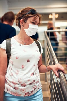 Woman going downstairs in public place inside wearing face mask to cover mouth and nose during pandemic coronavirus outbreak