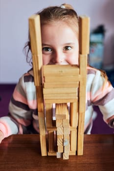 Little girl preschooler playing with wooden blocks toy building a tower. Concept of building a house