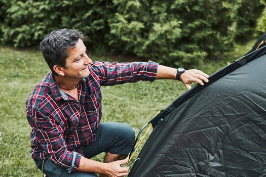 Man putting up a tent at camping during summer vacation. Preparing campsite to rest and relax. Spending vacations outdoors close to nature