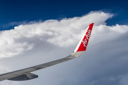 Bangkok Thailand - March 30, 2019: The trademark logo on the wing of AirAsia, a popular low-cost airline in many countries, is soaring in the sky against a backdrop of beautiful clouds.