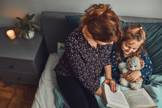 Mother reading book her daughter in bed before going to sleep. Reading stories before sleep. Bedtime stories for child
