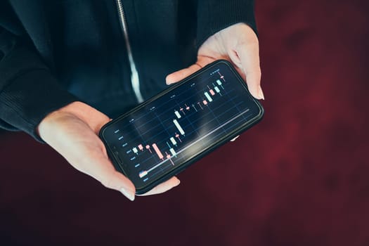 Person investing trading on stock cryptocurrency market using investing application on smartphone. Stock market investment in hand. Trader holding mobile phone looking at candle chart