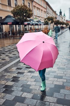 Little girl hiding behind big pink umbrella walking in a downtown on rainy gloomy autumn day
