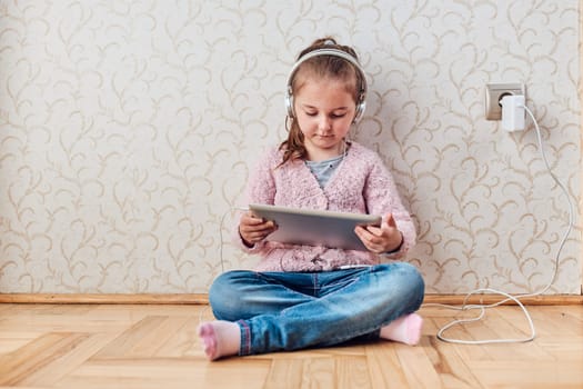 Little girl preschooler learning online solving puzzles playing educational games listetning to music and sounds using tablet and headpphones at home during pandemic quarantine