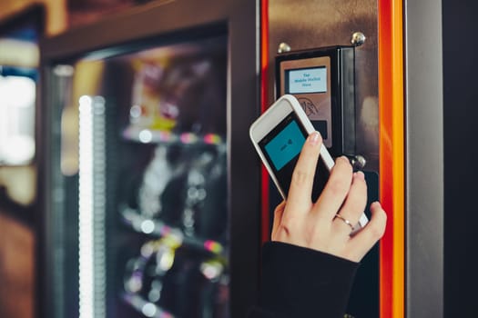 Woman paying for product at vending machine using contactless method of payment with mobile phone. Woman using new way of payments