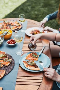 Family and friends having meal - pizza, salads, fruits and drinking white wine during summer picnic outdoor dinner in a home garden. Close up of people sitting at the table in a orchard in a backyard