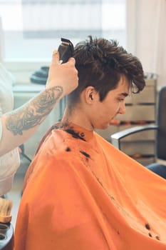 Hairdresser haircutting styling young man's hair in barbershop. Young woman working as a hairdresser in hair salon. Real people, authentic situations