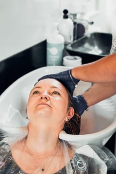 Hairdresser styling dyeing combing womans hair. Young woman working as a hairdresser in hair salon. Real people, authentic situations