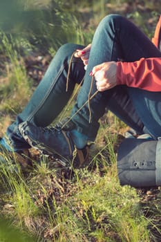 Young woman hiker with backpack lacing outdoor shoes during summer vacation trip in forest