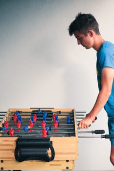 Young teenager boy playing table football with another player. Young people having fun, spending time together