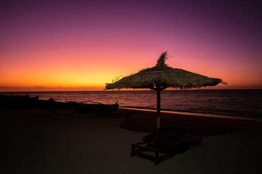Vibrant red sky at sunset on Anakao beach in Madagascar, with a tropical parasol and sun lounger, perfect escape from everyday life.