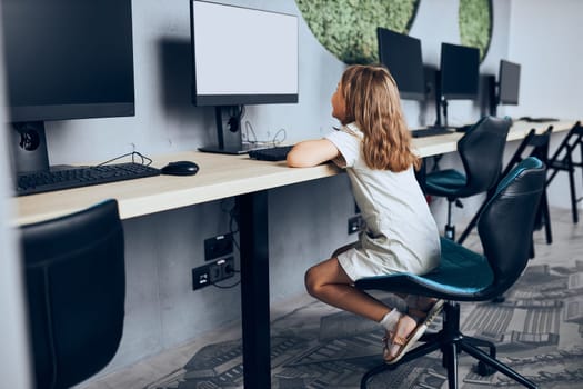Engaged schoolgirl learning to use technology in classroom at primary school. Child using computer on elementary computer science class. Smart little girl learning programming and coding at school. Child solving riddles on personal computer. Back to school