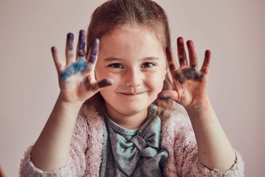 Little girl preschooler showing painted colourful hands. Child having fun making a stamps on sheet of paper with painted hands during an art class in the classroom
